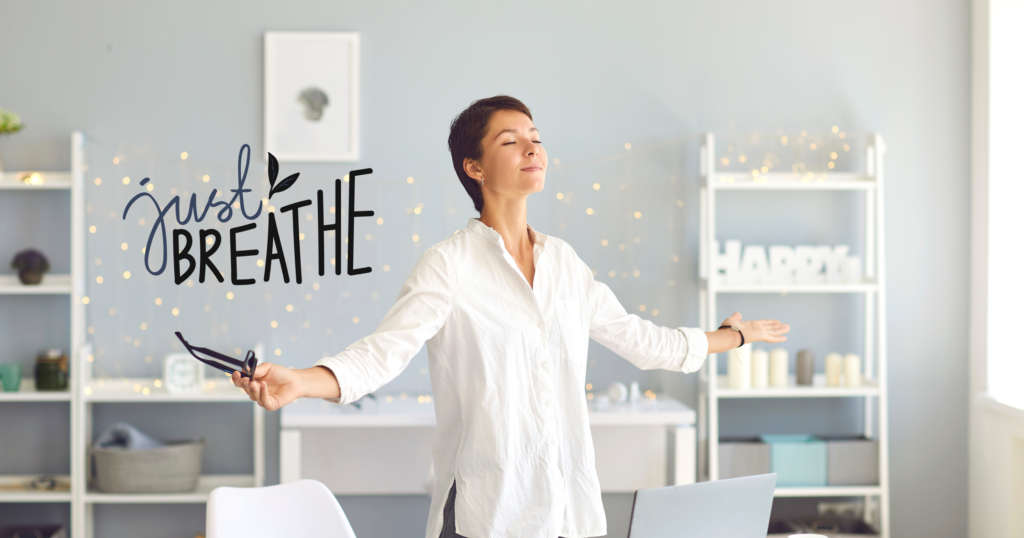 A woman is standing at her office desk, eyes closed, and taking a deep breath. The office environment is modern and well-lit, with a computer, notepad, and a few potted plants on the desk. The overall scene conveys a sense of tranquility and mindfulness amidst a busy workday, illustrating the concept of the "Just Breathe Meditation Game" in an office setting.